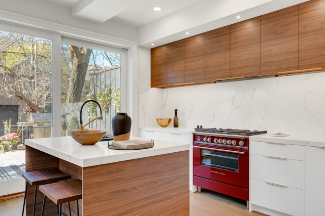 This is a bright kitchen with a red gas range, it lacks a range hood ventilation system